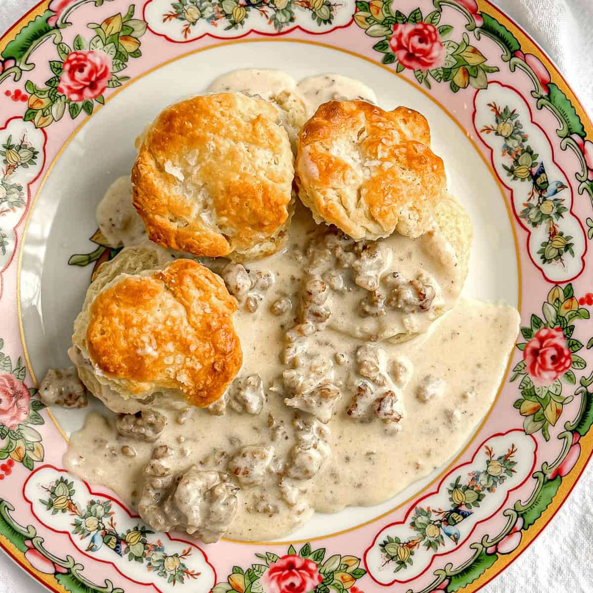 Biscuits and sausage gravy on a floral plate.