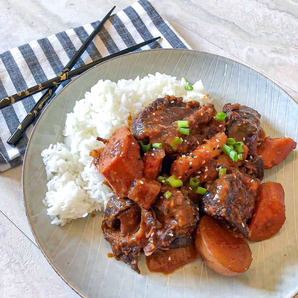 Korean stew and rice on a pale blue plate with chopsticks nearby.