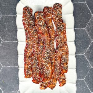 Everything seasoning candied bacon on a white plate.