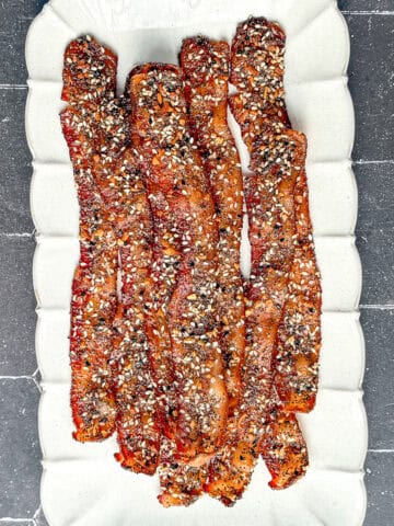 Everything seasoning candied bacon on a white plate.