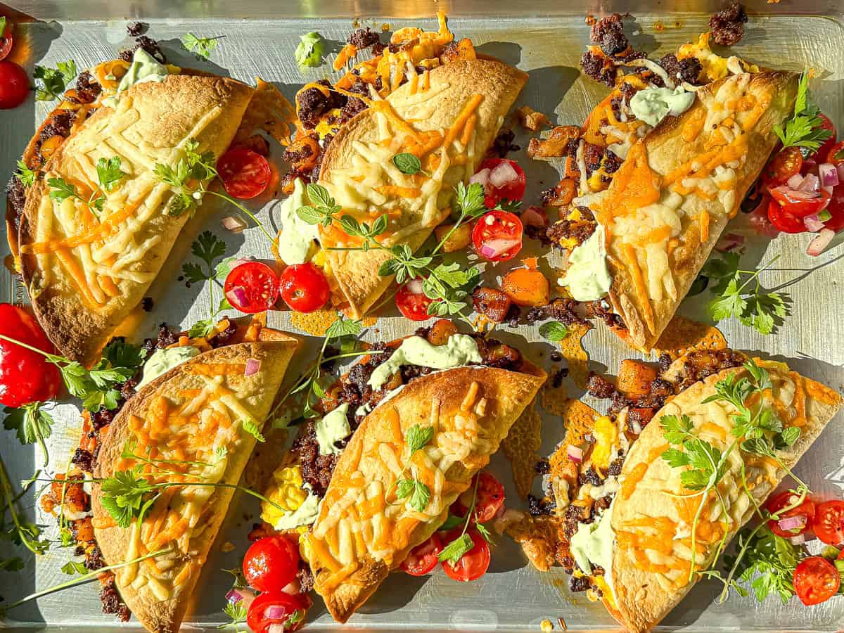 And chorizo and potato tacos on a sheet pan topped with tomatoes, cilantro, and avocado cream.