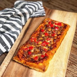 A sausage and pepper pizza on a rectangle of baked puff pastry