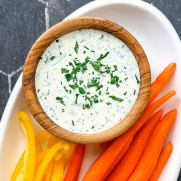 Ranch dressing in a wooden bowl on a white plate with cut vegetables.
