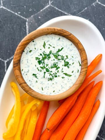 Ranch dressing in a wooden bowl on a white plate with cut vegetables.