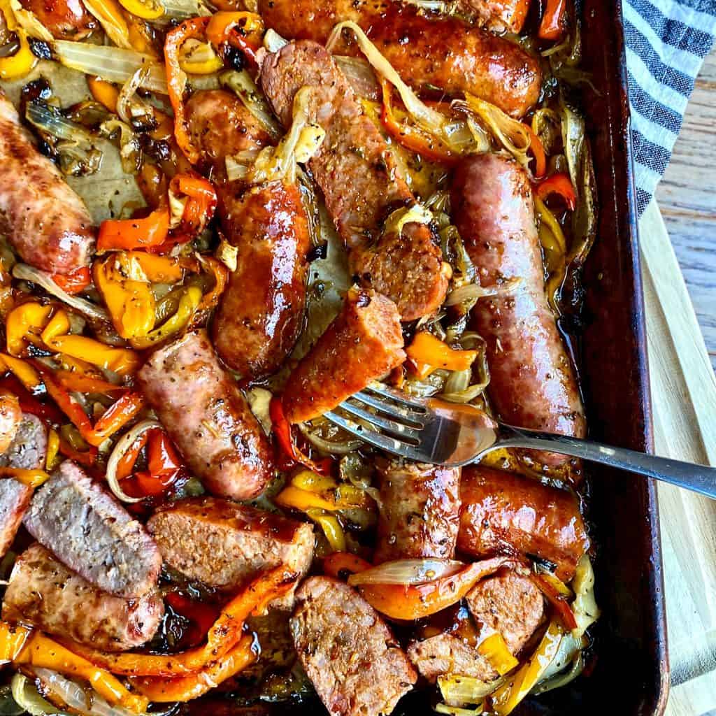 A sheet pan filled with oven roasted sausage, peppers, and onions.