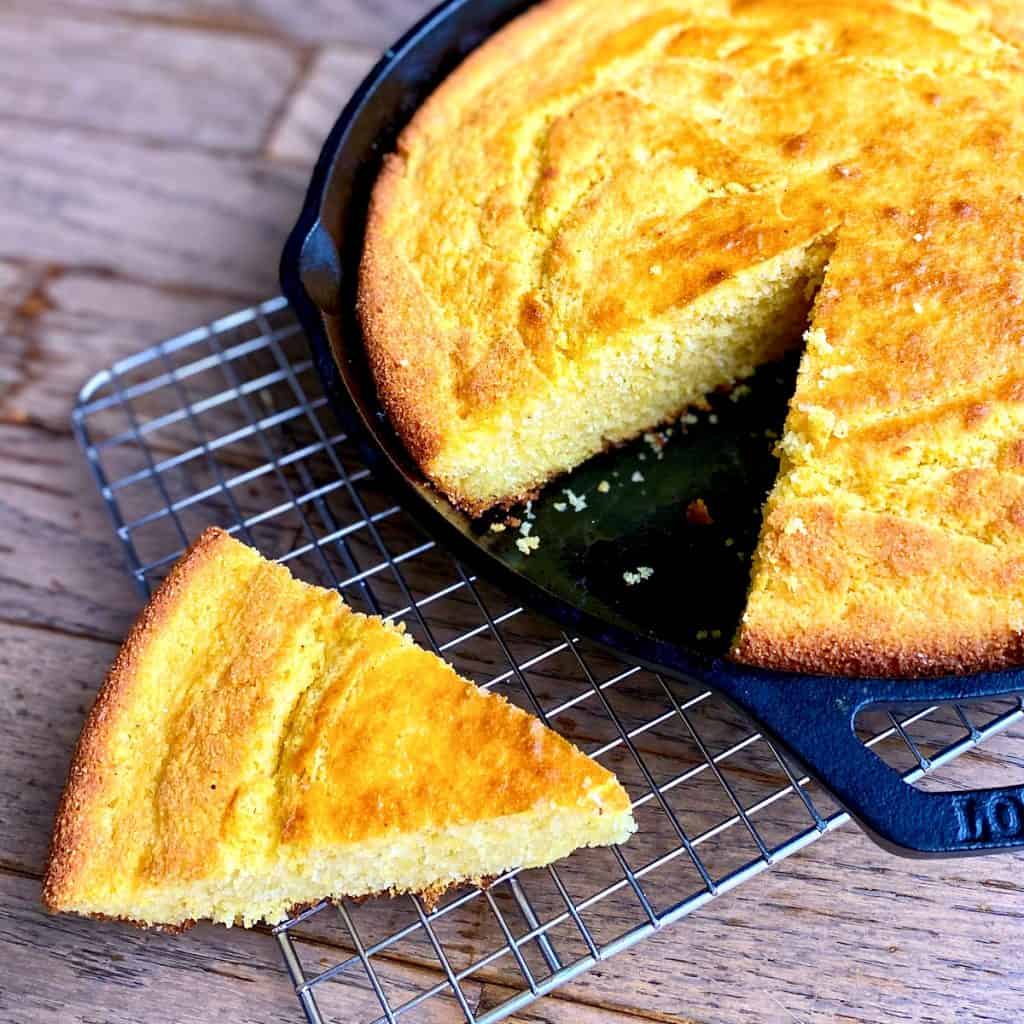 Cast iron skillet of cornbread with one triangular slice taken out.
