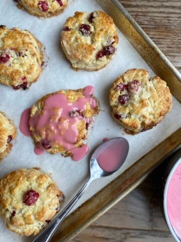 Sheet pan with cranberry orange scones and a spoon that has drizzled blood orange glaze over one of the scones.