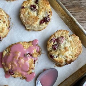 Sheet pan with cranberry orange scones and a spoon that has drizzled blood orange glaze over one of the scones.