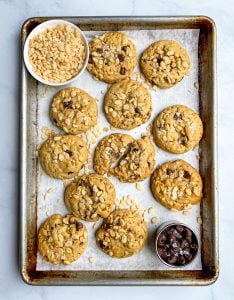 Peanut Butter Rice Krispie Cookies on a quarter sheet pan with bowls of crispy rice cereal and chocolate chips.