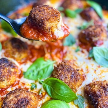 Cast iron pan with chicken parmesan meatballs, marinara sauce, cheese, and basil.