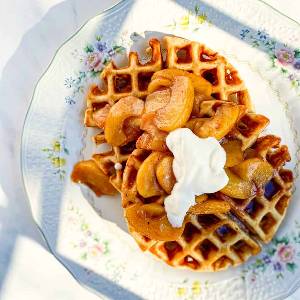 Chai Spiced Waffles on a flowered plate topped with Maple Cinnamon Apples ands softly whipped Cream