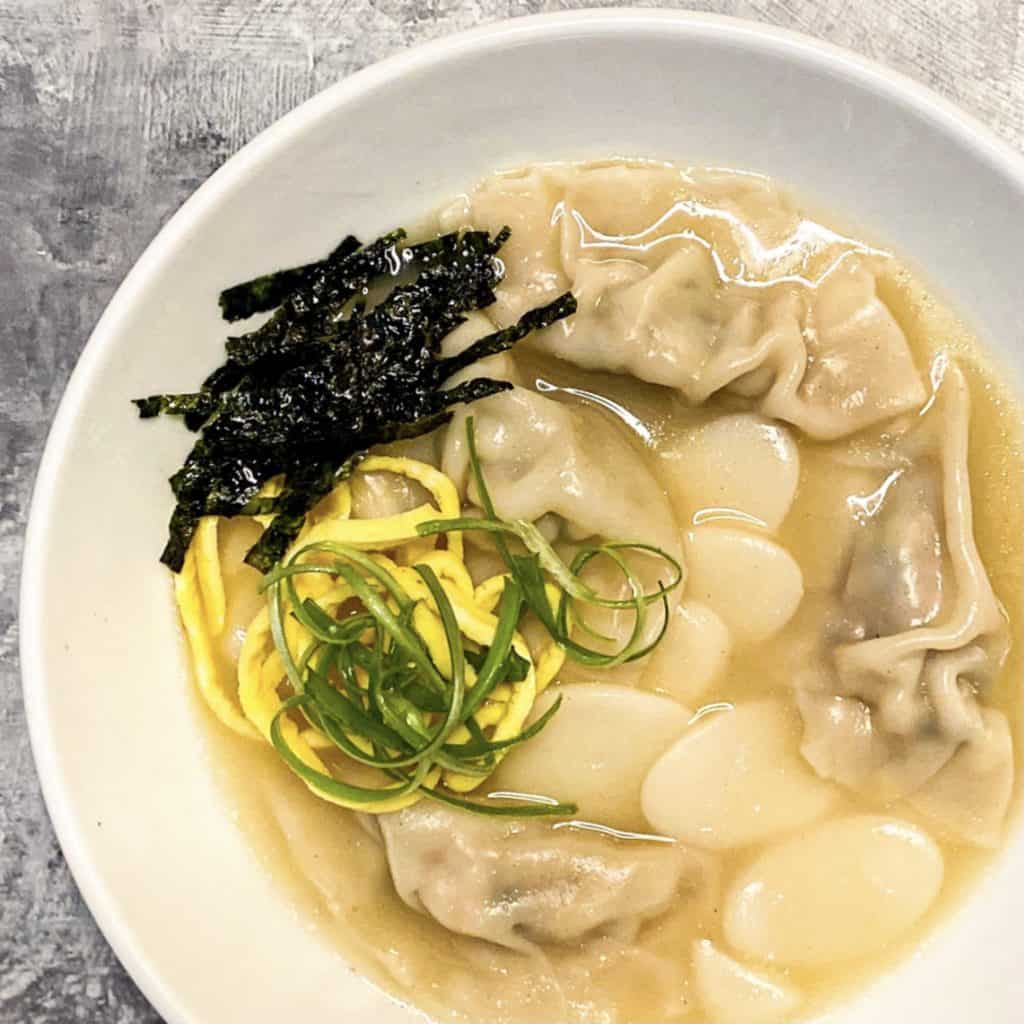 Tteok Mandu Guk (Korean Rice Cake and Dumpling Soup) with garnish of sliced seaweed, egg, and green onion