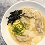 Tteok Mandu Guk (Korean Rice Cake and Dumpling Soup) with garnish of sliced seaweed, egg, and green onion