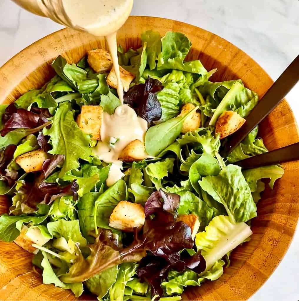 Pouring Creamy Caesar Dressing over a bed of greens.