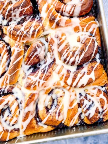 A large baking tray filled with Orange-Blueberry Cinnamon Rolls and drizzled in orange glaze