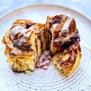 One Orange-Blueberry Cinnamon Roll on a white plate, cut open to show the blueberry cinnamon swirls inside.