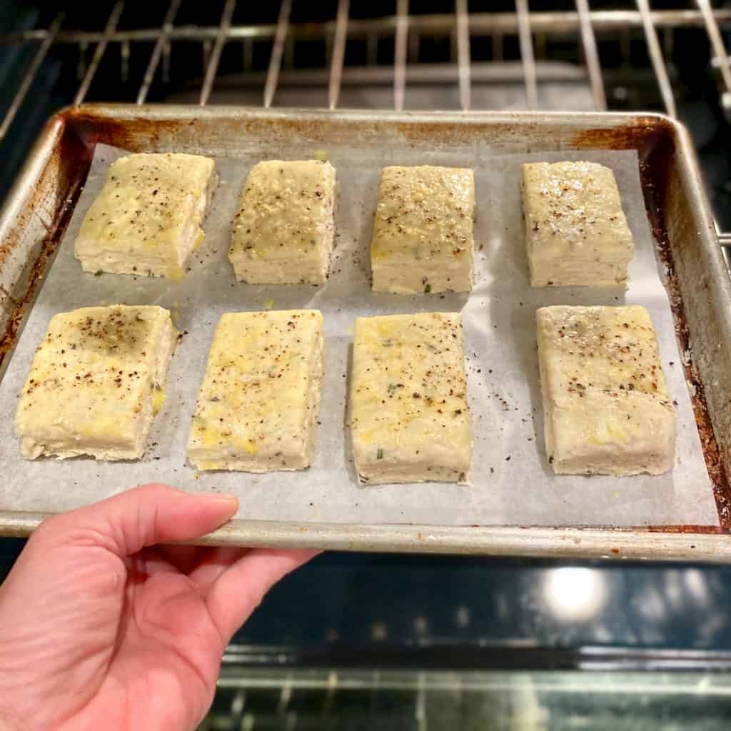 Placing a sheet tray of Rosemary Romano Cheese biscuits into the oven
