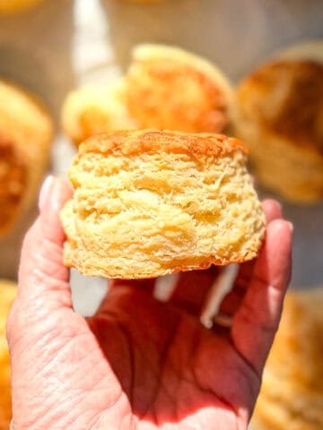 Hand holding a flaky buttermilk biscuit.