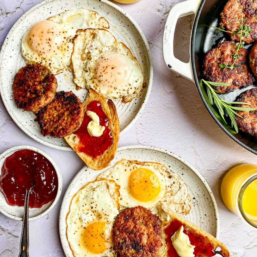 Eggs and toast on small white plates with patties of ground breakfast sausage.