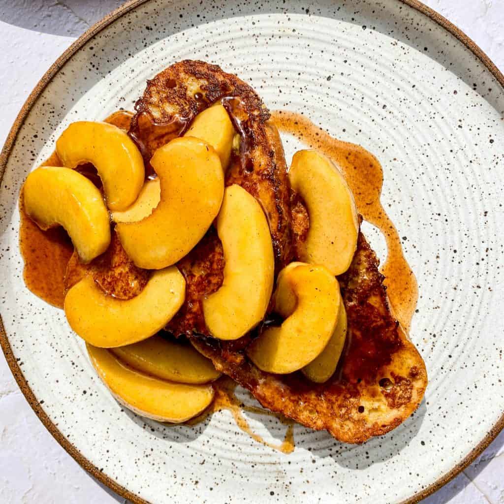 White plate with french toast, topped with maple cinnamon simmered apples.