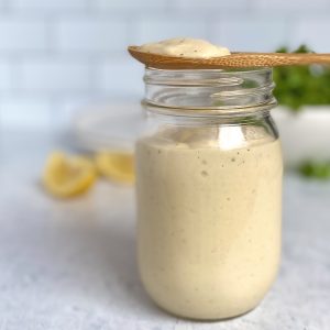 Mason jar with creamy caesar dressing with lemons and lettuce in the background.