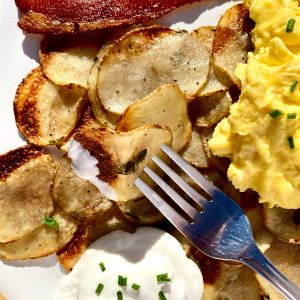 Crispy sheet pan potatoes with chive sour cream, scrambled eggs, and bacon on a white plate.