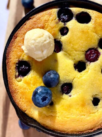 Cast iron skillet with blueberry cornbread and a scoop of honey butter.