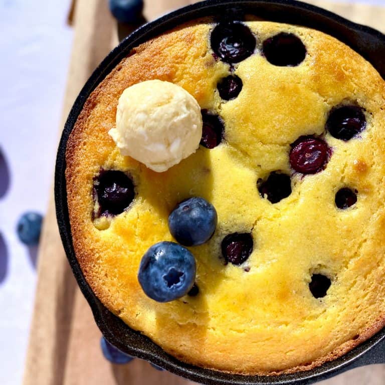 Cast iron skillet with blueberry cornbread and a scoop of honey butter.