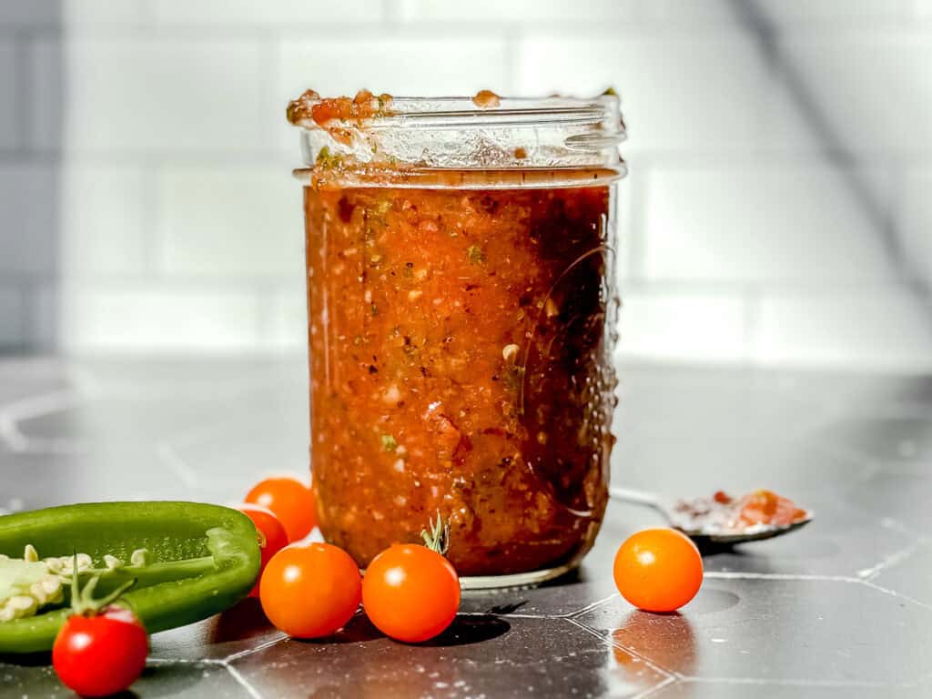 Mason jar of homemade salsa on a black counter with a white backdrop.
