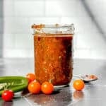 Mason jar of homemade salsa on a black counter with a white backdrop.