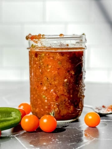 Mason jar of homemade salsa on a black counter with a white backdrop.
