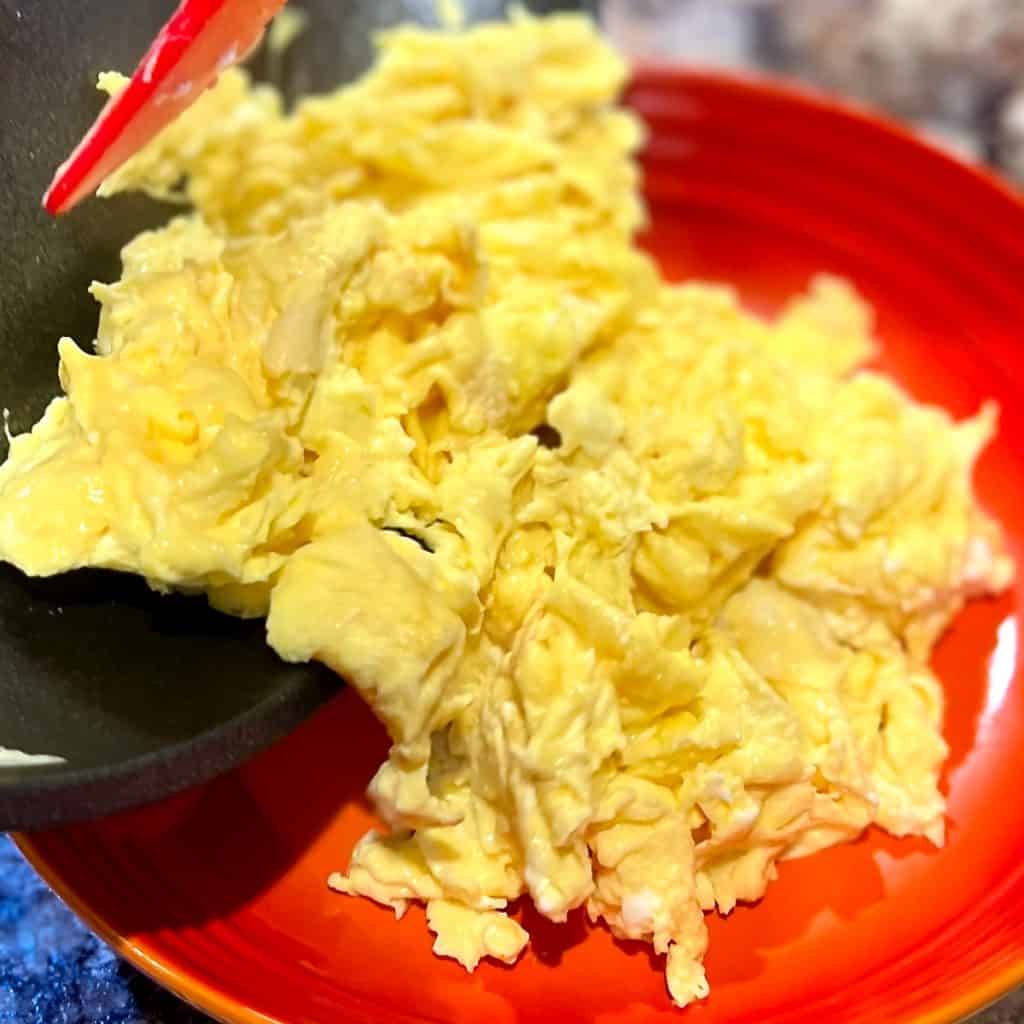 Removing scrambled eggs from nonstick pan to an orange plate.