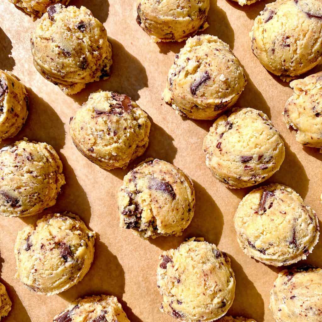 Balls of chocolate chip cookie dough, on parchment paper.