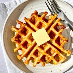 A buttermilk waffle and a pat of butter on a white plate.