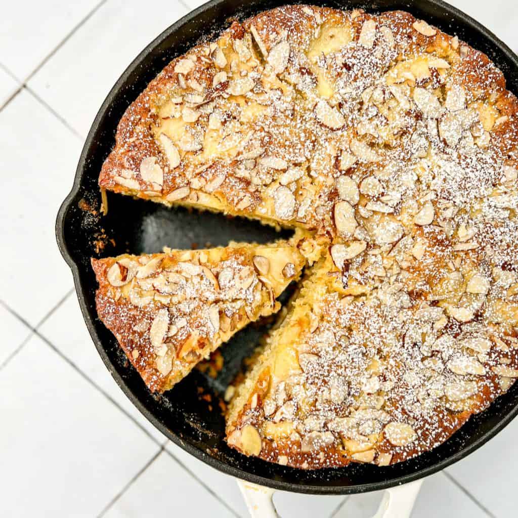 A cast iron pan containing a sliced French Apple Cake.
