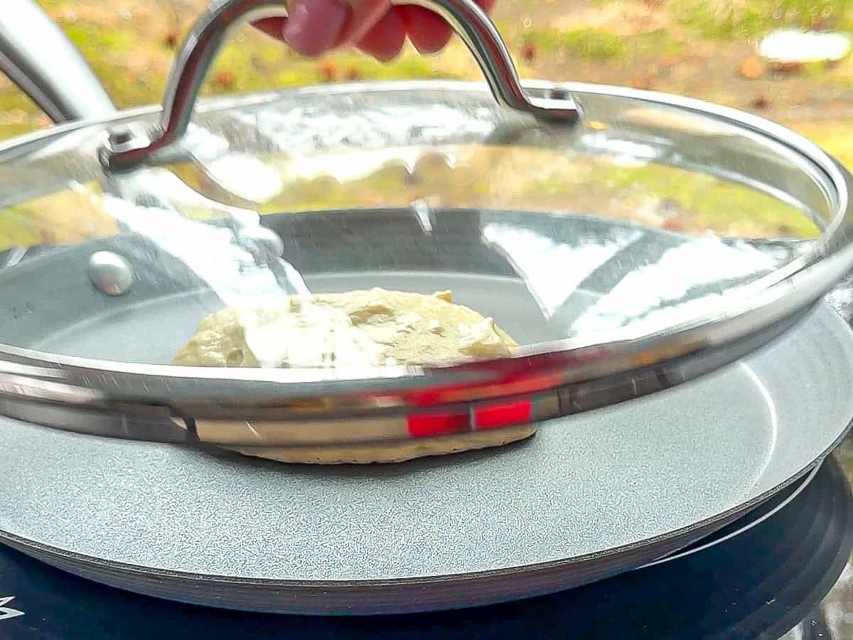 Placing a lid on a pan while cooking pancakes.