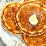 3 pancakes on a flowered plate with butter and syrup and a black serving spatula.