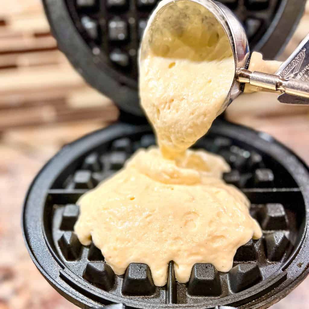 Scooping waffle batter into hot waffle maker.