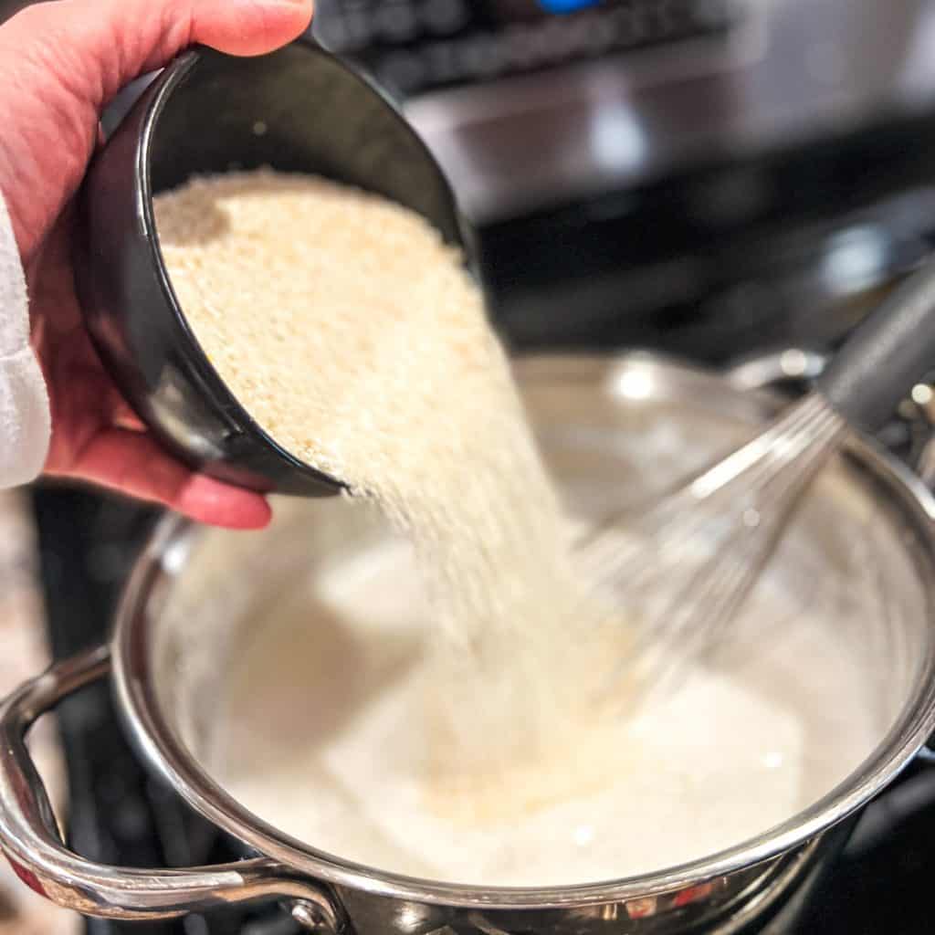 Adding grits to boiling milk in a medium saucepan.