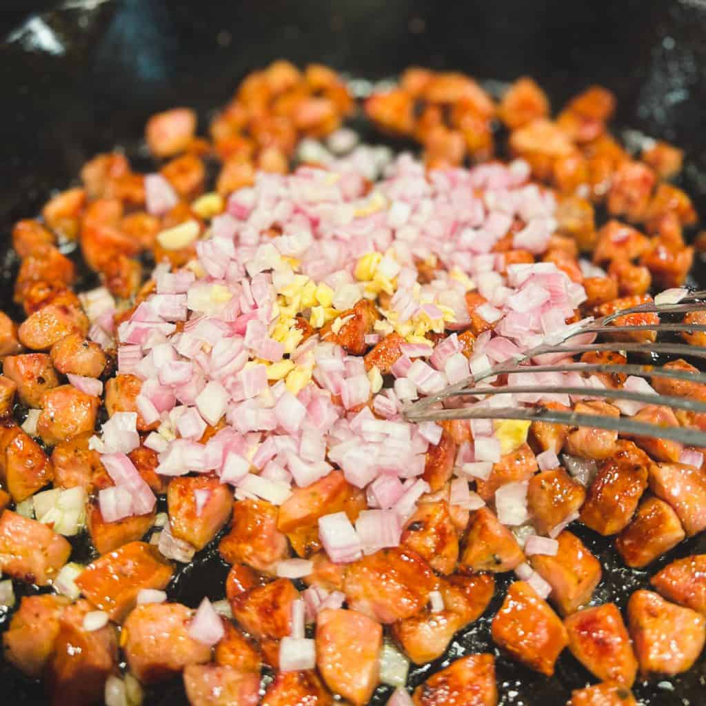 Sauteed andouille sausage with shallots and garlic in a cast iron pan.