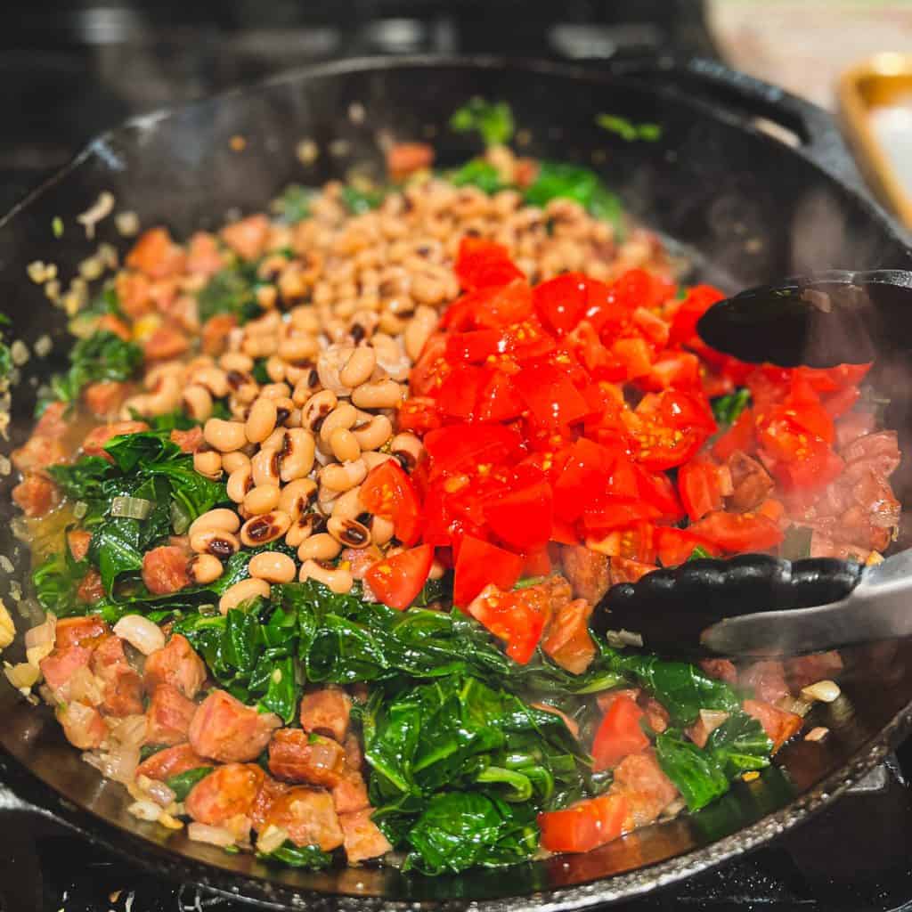Cast iron skillet with Sauteed collards, andouille sausage and black eyed peas, with tomatoes.