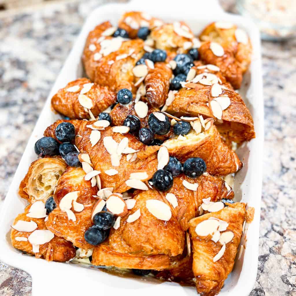 White casserole dish containing croissants, blueberries, and almonds.