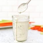 A spoon hovering over an overflowing jar of ranch dressing.
