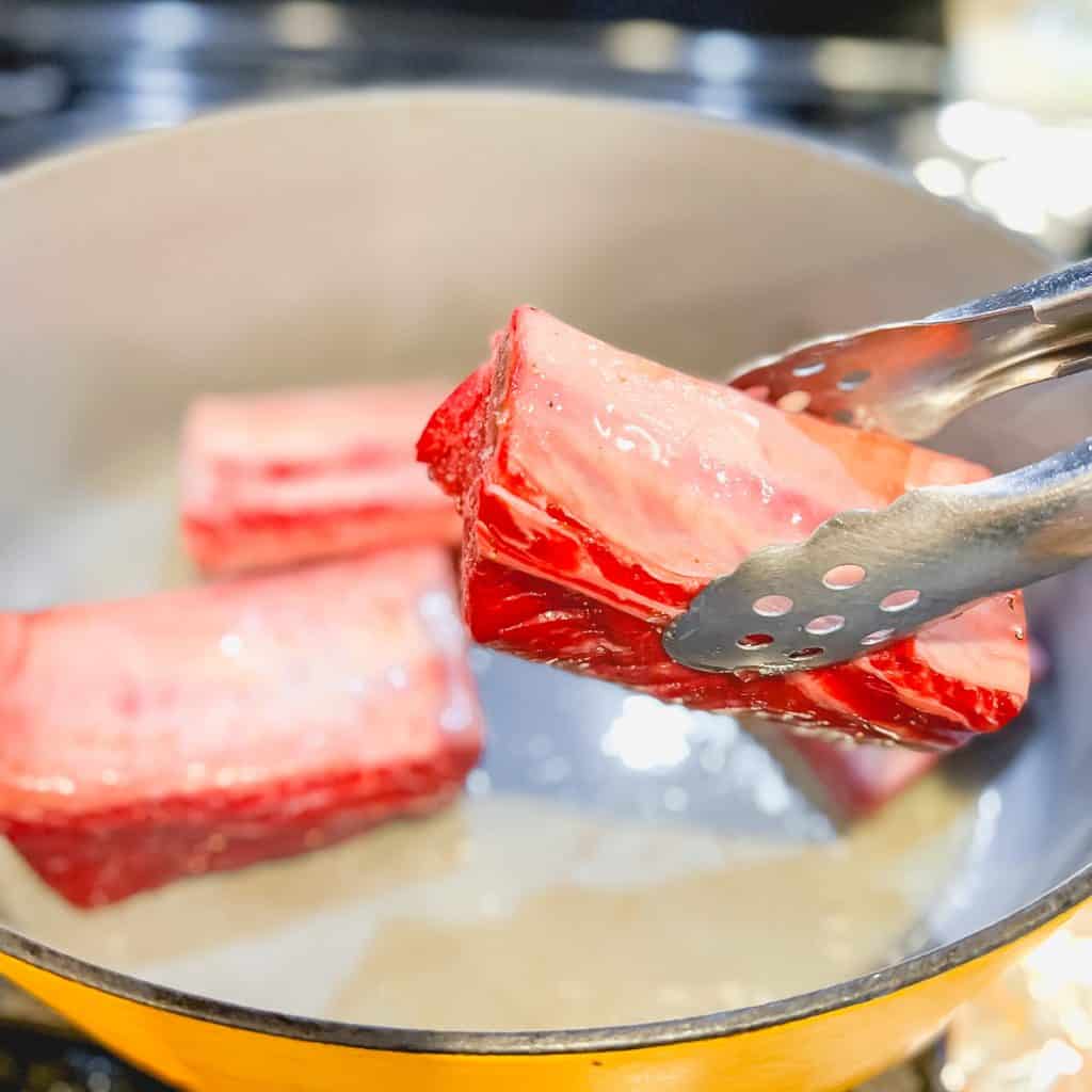 Placing raw short rib into pan to sear.