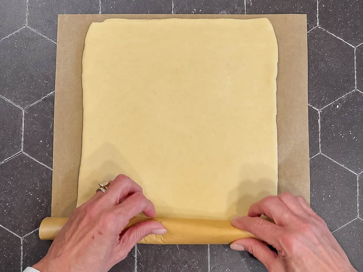 Rolling puff pastry in parchment paper.