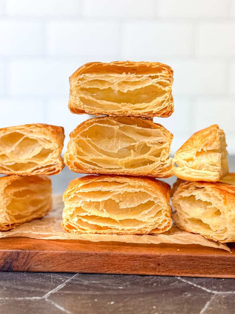 Stacks of baked rough puff pastry on a wooden cutting board.