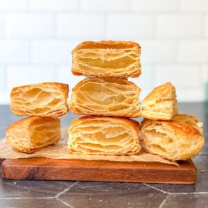 Stacks of baked rough puff pastry on a wooden cutting board.