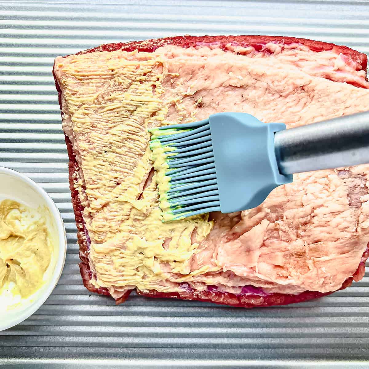 Brushing mustard on uncooked corned beef.