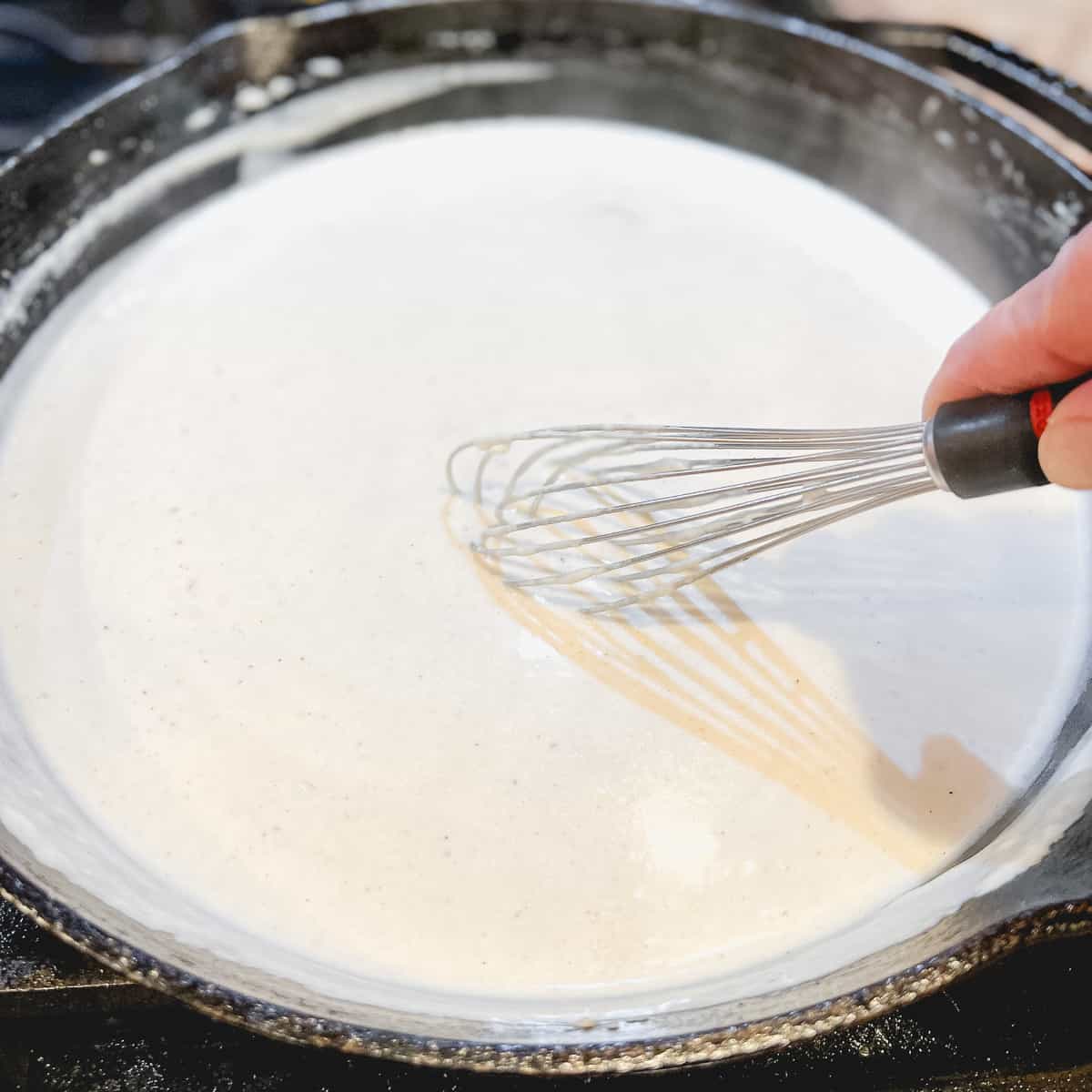 Whisking country gravy in a cast iron pan.