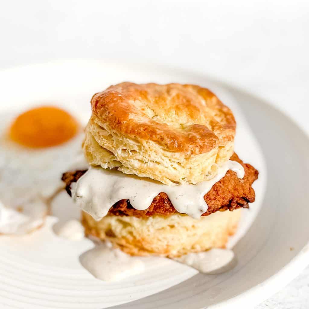 Chicken Fried Steak Biscuit with country gravy with a fried egg on a white plate.